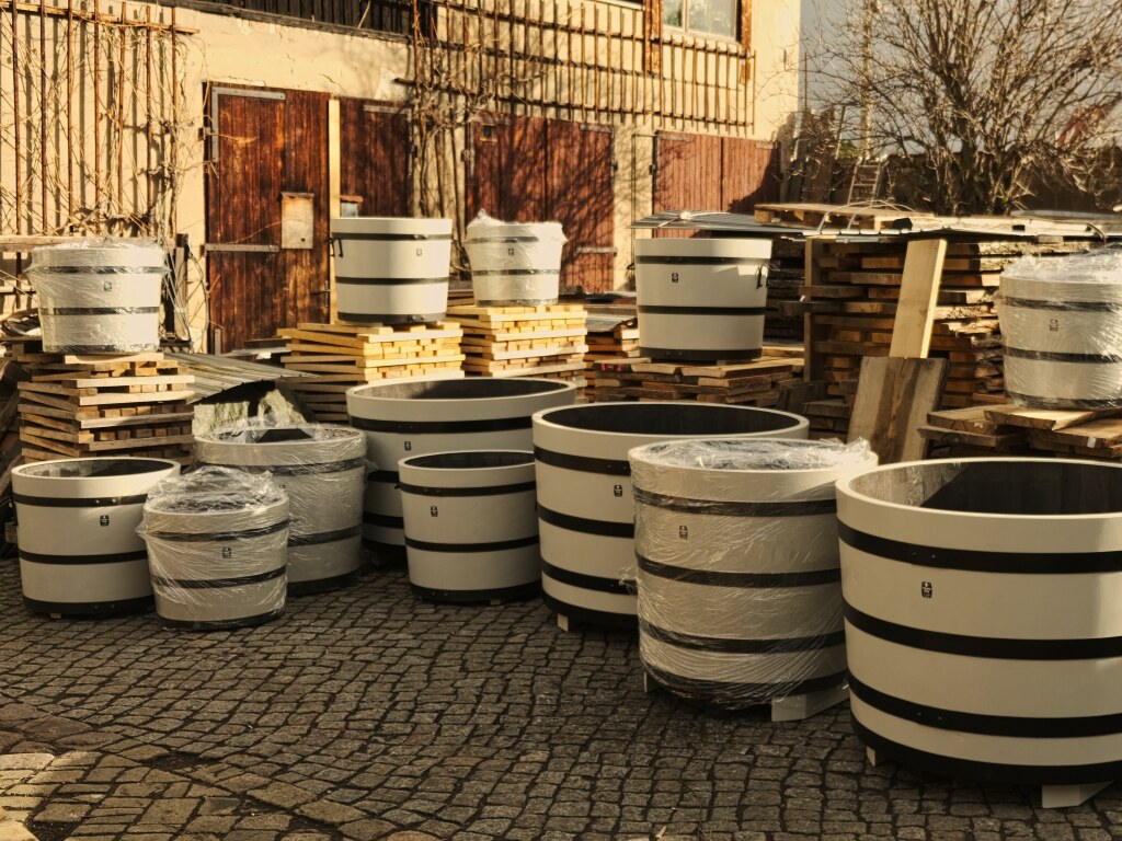 Viele und unterschiedlich große auf dem Werkstatthof aufgestellte farbige Pflanzkuebel aus Holz mit schwarz galvanisierten Reifen