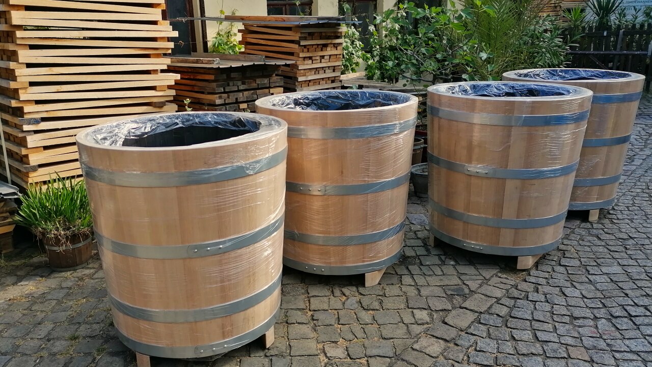 vier mit Strechfolie eingepackte große Pflanzbottiche aus Holz